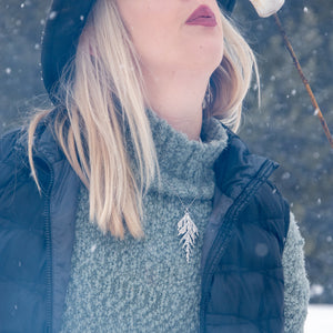 Woman wearing handmade silver cedar necklace while blowing on hot marshmallow in winter