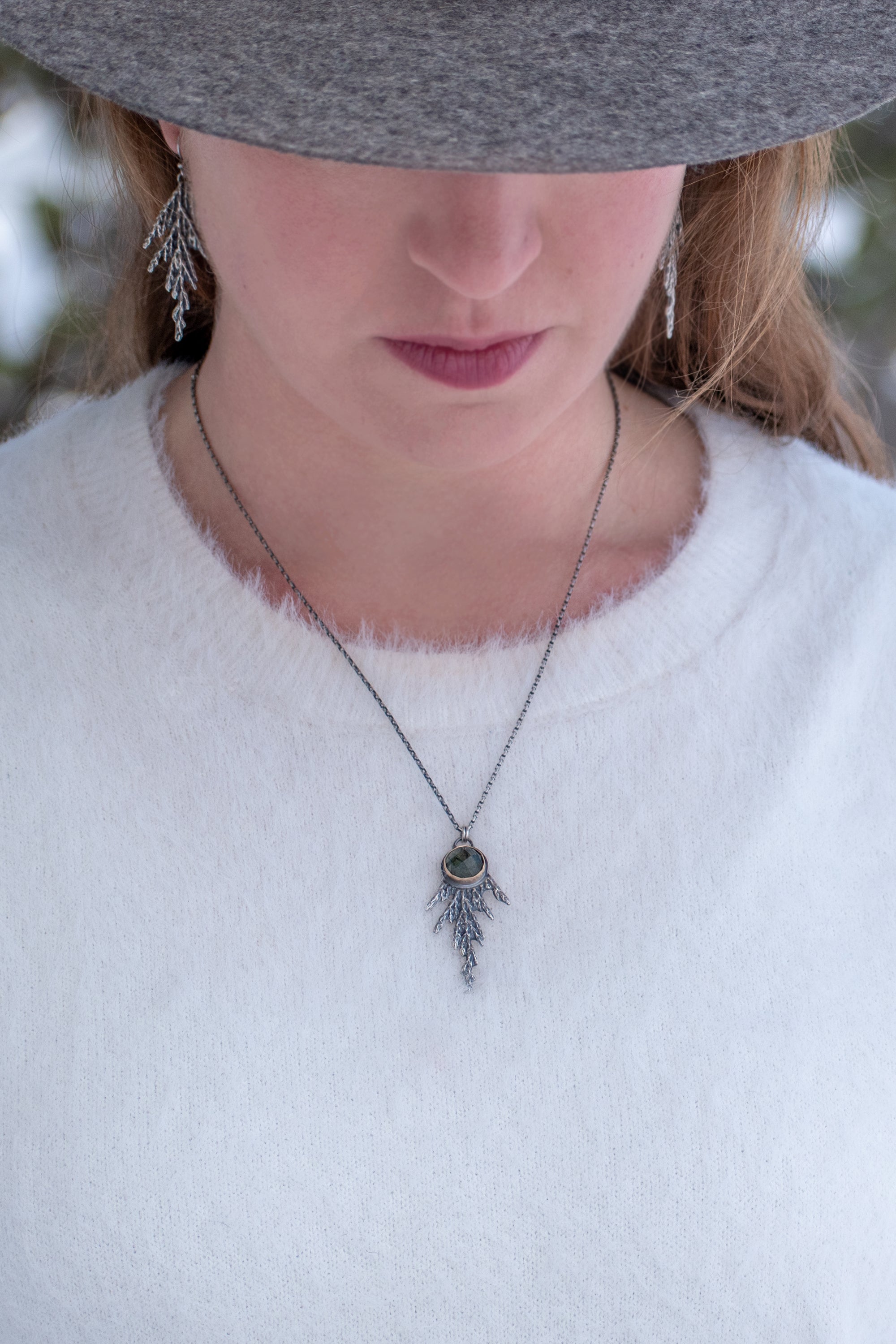 Woman wearing handmade sterling silver cedar necklace with green rutile stone set in 14k gold