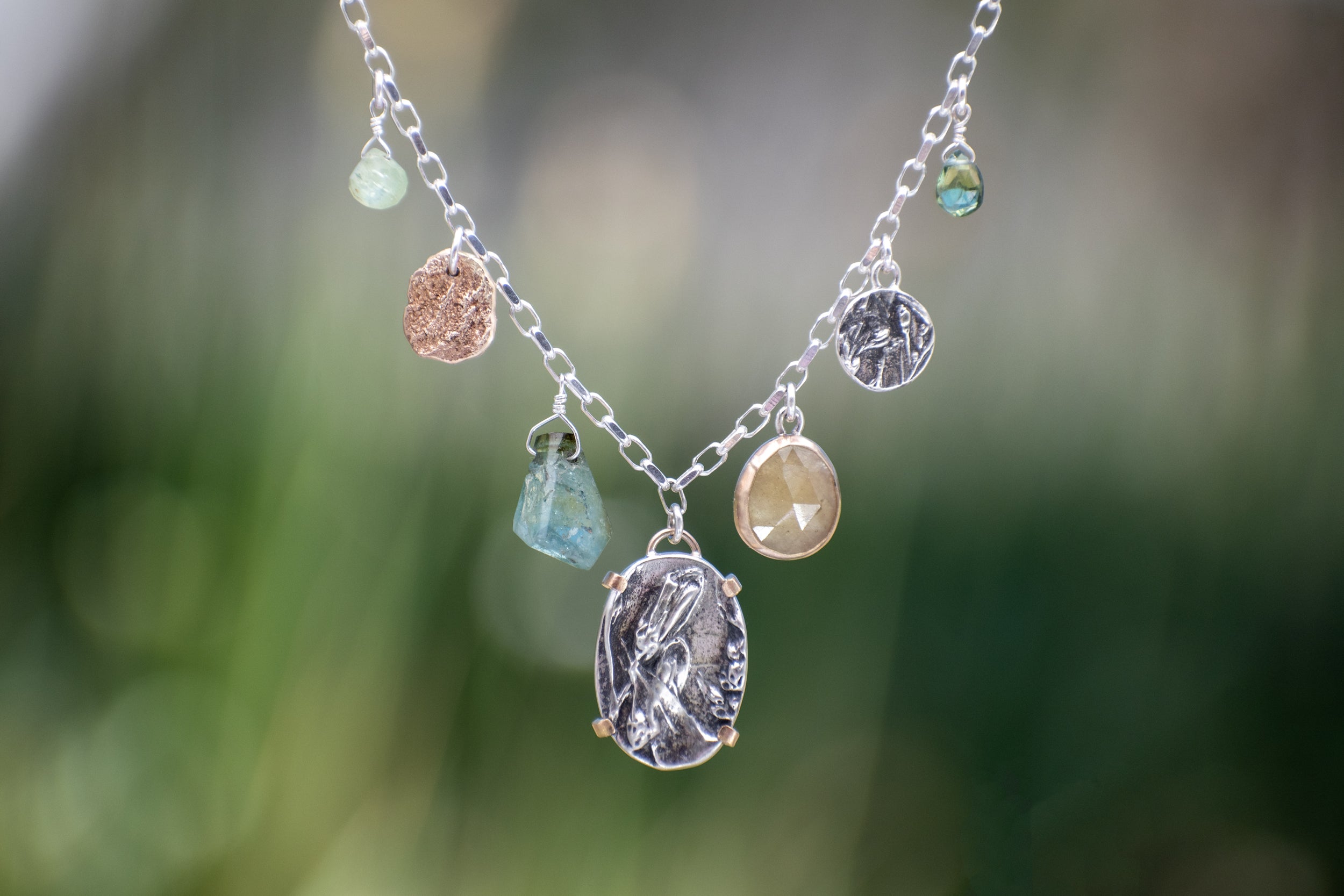 Nature-inspired Wild Meadow Charm Necklace in sterling silver and 14k gold with wildflower botanical textures, green sapphire, tourmaline, kyanite and green garnet gemstones.