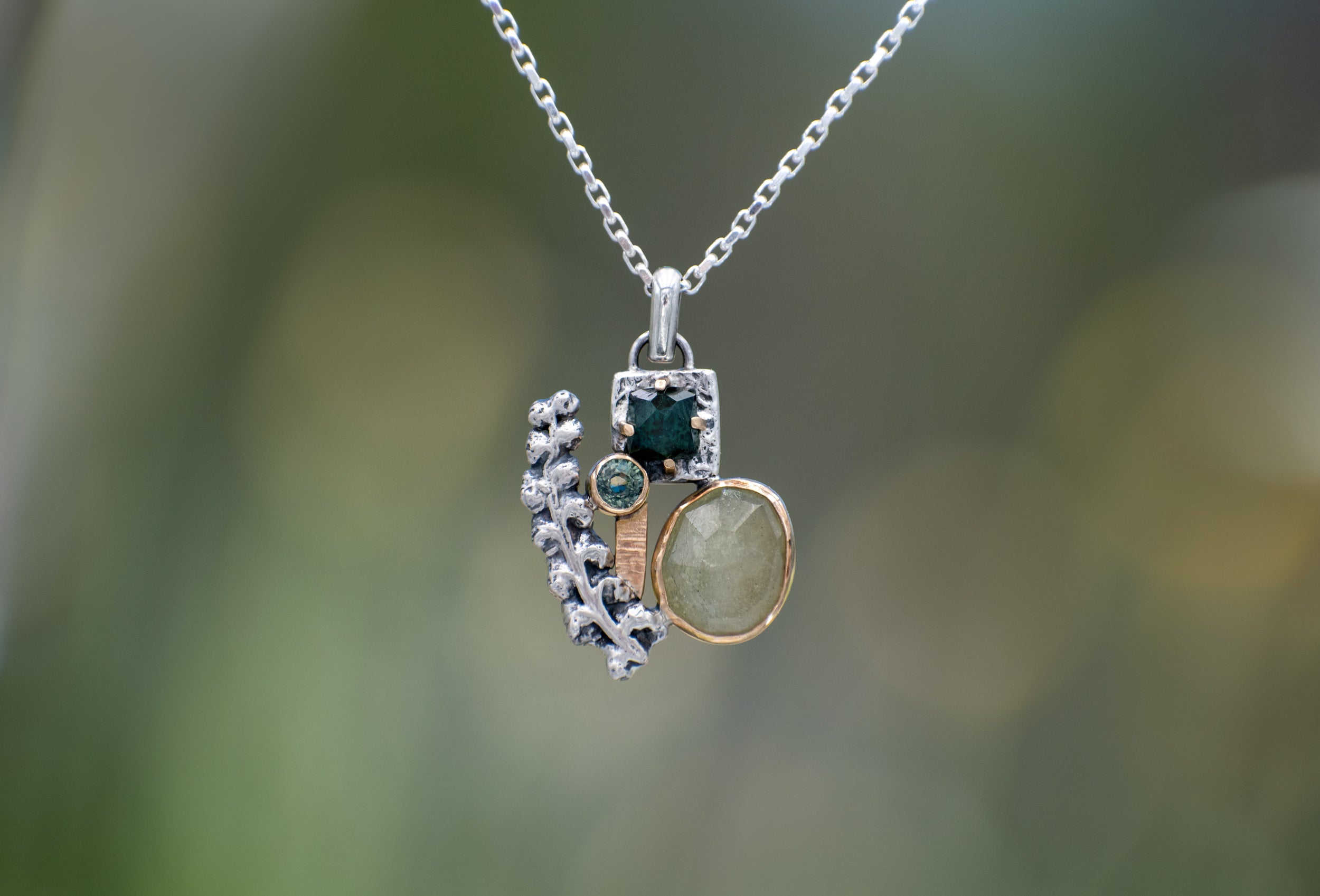 Nature-inspired Wild Meadow Cluster Necklace in sterling silver and 14k gold with sensitive fern botanical texture and two green sapphire gemstones.