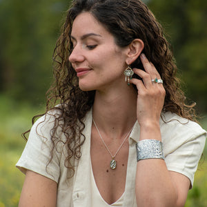 Woman in wild field wearing Oval Wild Meadow Earrings in sterling silver and 14k gold with botanical textures and dangling tourmaline, green garnet, aquamarine and freshwater pearl gemstones.