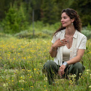 A model in a wild field wearing Oval Wild Meadow Earrings in sterling silver and 14k gold with botanical textures and dangling tourmaline, green garnet, aquamarine and freshwater pearl gemstones.