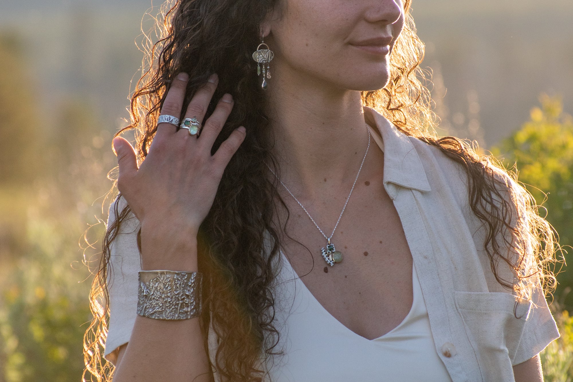 model wearing Nature-inspired Wild Meadow Cluster Necklace in sterling silver and 14k gold with sensitive fern botanical texture and two green sapphire gemstones.