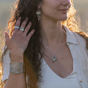 model wearing Nature-inspired Wild Meadow Cluster Necklace in sterling silver and 14k gold with sensitive fern botanical texture and two green sapphire gemstones.