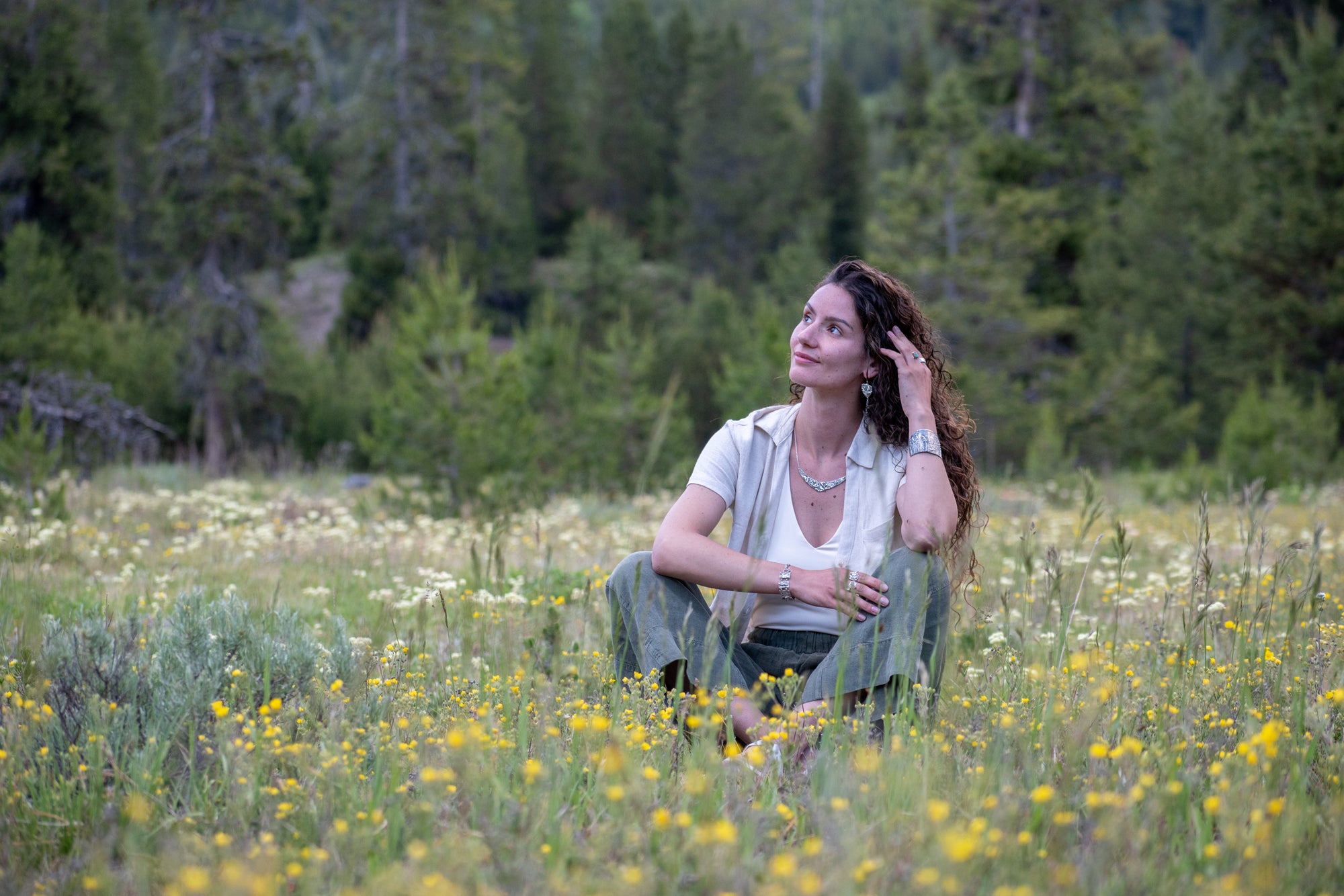 Woman in meadow wearing Wild Meadow Triangle Earrings in sterling silver with sagebrush, goldenrod, lupine and wild grass botanical textures, dangling silver chains and green diamond, kyanite and green garnet gemstones.