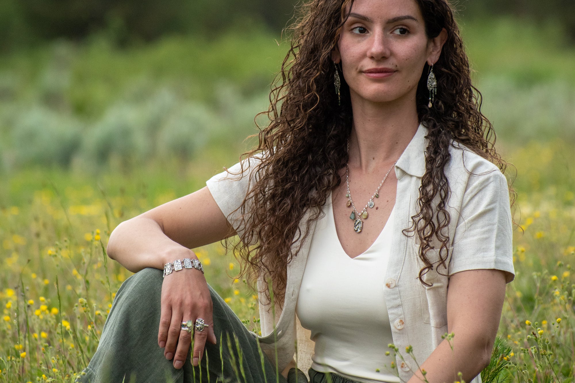 Model wearing Wild Meadow Wing Earrings in sterling silver and 14k gold with lupine, goldenrod and sage botanical textures, dangling tourmaline, kyanite, aquamarine, green garnet, green diamond and freshwater pearl gemstones.
