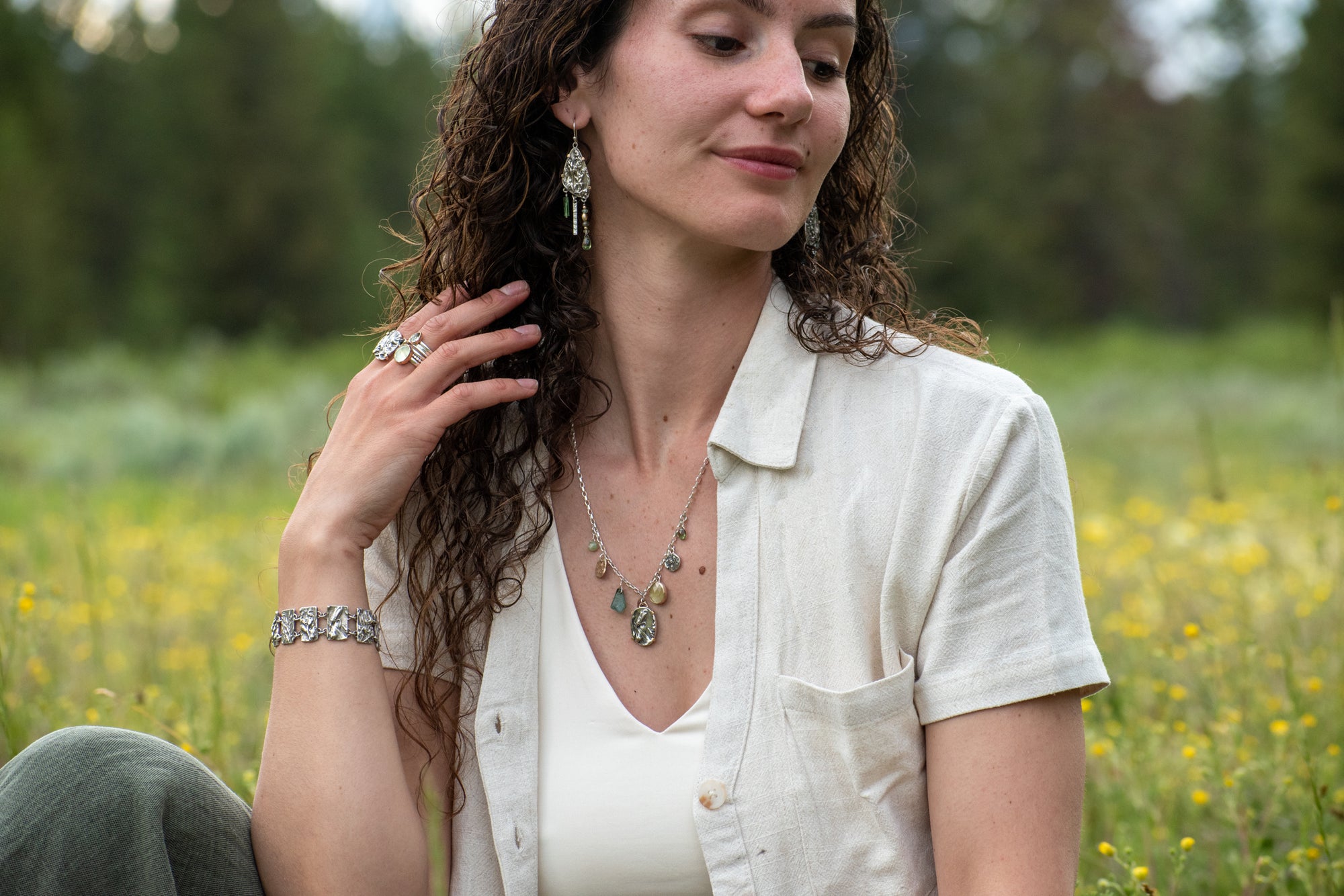 model wearing Wild Meadow Wing Earrings in sterling silver and 14k gold with lupine, goldenrod and sage botanical textures, dangling tourmaline, kyanite, aquamarine, green garnet, green diamond and freshwater pearl gemstones.