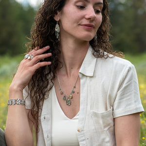 model wearing Wild Meadow Wing Earrings in sterling silver and 14k gold with lupine, goldenrod and sage botanical textures, dangling tourmaline, kyanite, aquamarine, green garnet, green diamond and freshwater pearl gemstones.
