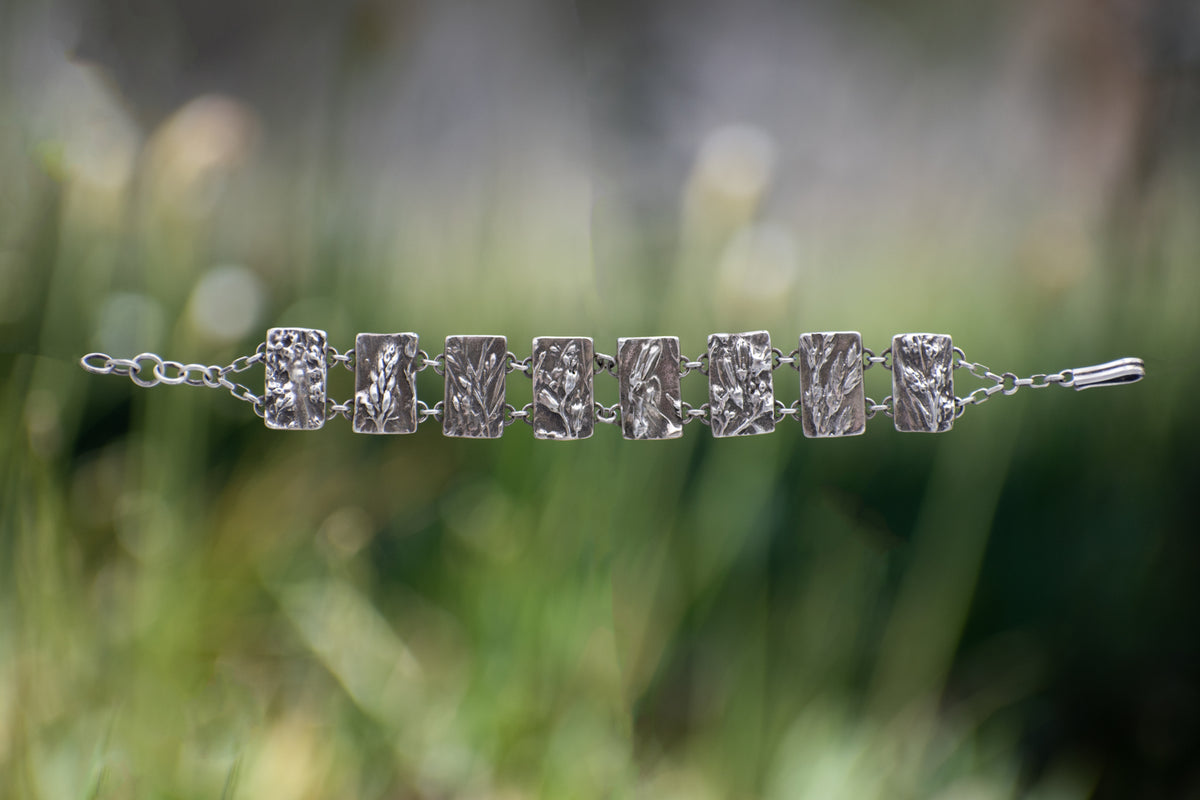 Nature-inspired Wild Meadow Bracelet in oxidized sterling silver with linked botanical panels featuring layered wildflower textures from lupine, sagebrush, goldenrod and wild grasses.