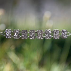 Nature-inspired Wild Meadow Bracelet in oxidized sterling silver with linked botanical panels featuring layered wildflower textures from lupine, sagebrush, goldenrod and wild grasses.