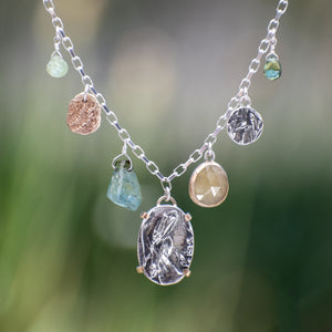 Nature-inspired Wild Meadow Charm Necklace in sterling silver and 14k gold with wildflower botanical textures, green sapphire, tourmaline, kyanite and green garnet gemstones.