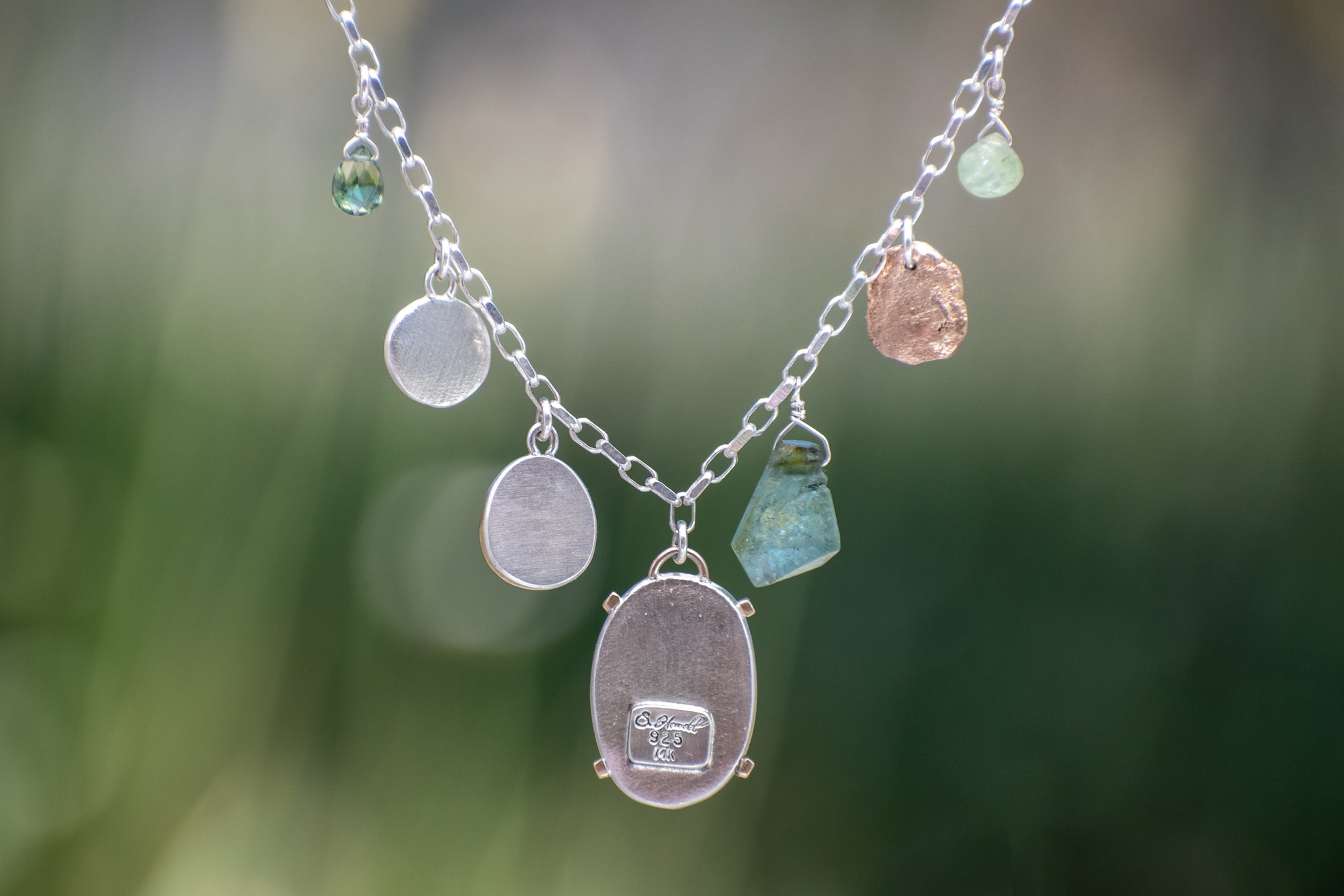 Nature-inspired Wild Meadow Charm Necklace in sterling silver and 14k gold with wildflower botanical textures, green sapphire, tourmaline, kyanite and green garnet gemstones.