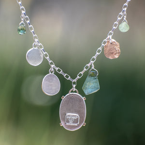 Nature-inspired Wild Meadow Charm Necklace in sterling silver and 14k gold with wildflower botanical textures, green sapphire, tourmaline, kyanite and green garnet gemstones.
