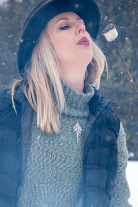 Woman wearing handmade silver cedar necklace while blowing on hot marshmallow in winter